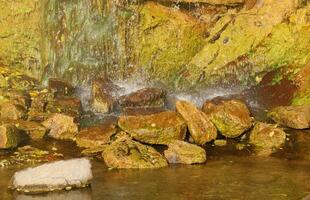 Waterfall among stones and trees. Close-up of boulders in water. Huge stones in green moss. Beautiful landscape of fast waterfall with small whirlpools photo