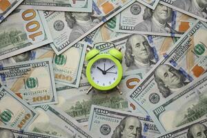 Alarm clock on hundred dollar bills banknotes. Background of time management, business photo