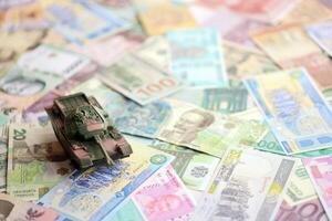 Small green tank on many banknotes of different currency. Background of war funding photo