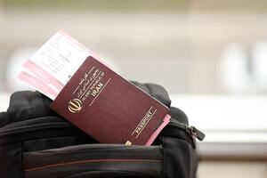 Red Islamic Republic of Iran passport with airline tickets on touristic backpack photo