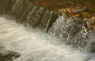 una pequeña cascada. la diferencia de altura del flujo de agua en el río está equipada con troncos de madera redondos foto