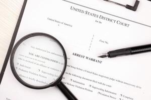 District Court Arrest Warrant court papers on A4 tablet lies on office table with pen and magnifying glass photo