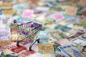 Supermarket trolley on many banknotes of different currency. Background of shopping worldwide photo