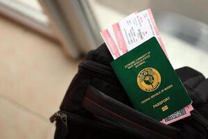 Green Nigerian passport with airline tickets on touristic backpack photo