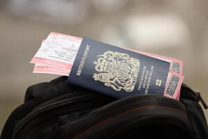 Blue British passport with airline tickets on touristic backpack photo