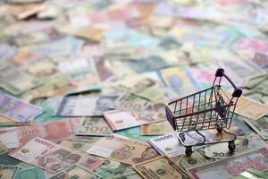 Supermarket trolley on many banknotes of different currency. Background of shopping worldwide photo