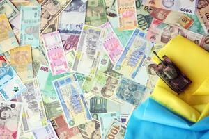 Toy tank on Ukrainian flag on many banknotes of different currency. Background of war funding photo