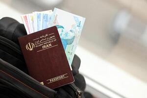 Red Islamic Republic of Iran passport with money and airline tickets on touristic backpack photo