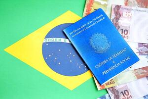 Brazilian work card and social security blue book and reais money bills on flag of Federative Republic of Brazil photo