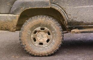 Wheel closeup in a countryside landscape with a mud road. Off-road 4x4 suv automobile with ditry body after drive in muddy road photo