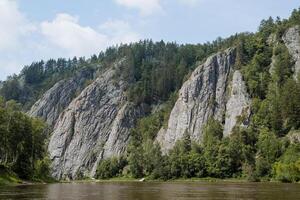 Rocks on a mountain river, a beautiful mountain landscape on a sunny day, a gray rock, a taiga forest, muddy water. photo