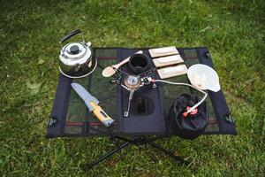 Folding table for camping, tourist dishes stand on the table, gas burner, cutlery, iron kettle, butter sandwiches, breakfast on a hike. photo