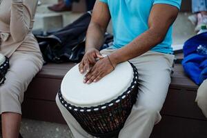 el negro manos de un afroamericano jugar étnico música en un djamba, un cubierto de cuero el plastico tambor, un africano musical instrumento. foto
