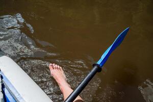 A man's foot sticks out in the water, a paddle for kayaking, a man rafting a canoe on a mountain river, water sports, a summer vacation on the water. photo