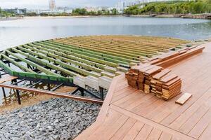 The construction of the city embankment, the pond in the park, the wooden pier construction site, the boards are sawn in a stack, the resting place of the townspeople. Road for walking. photo