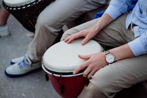 manos sostener un djembe tambor, un chico obras de teatro un africano tambor, un oficina trabajador es un músico, un reloj en su muñeca. foto