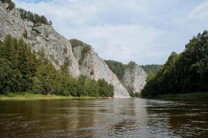 Forested cliffs stretch along the mountain river, a tourist attraction is a water route for rafting, a summer vacation on the river. photo