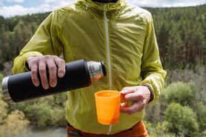 el concepto de al aire libre recreación en pie, un detener para almuerzo en un caminata mediante el bosque, bebida delicioso té desde un termo, un vacaciones en el montañas, turista platos. foto