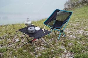 Camping in nature in the mountains, folding table, folding chair, tourist utensils for cooking on the burner, mini kettle, pot. photo