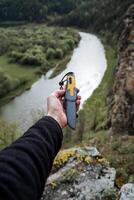 The knife lies in the hand against the background of nature, the river flows at the bottom of the mountain, tourist equipment, equipment on a hike, traveling alone. photo