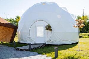 White fabric tent, white camping structure, plastic door to enter the premises, city park, morning sun photo