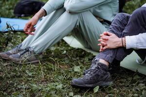 un niña se sienta en el suelo participación su rodillas con su manos, trekking botas para un caminata en el bosque, dos personas en el suelo sesión, senderismo. foto