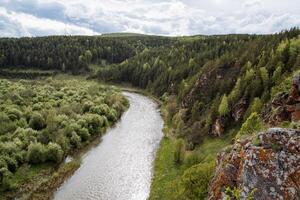 The nature of Russia, the taiga area, the reserved land, the landscape of the mountain river, the orange rock against the background of the green forest, the overcast sky. photo