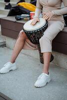 Beautiful women's legs in white sneakers, the girl plays the African drum djemba, yellow nail polish, a blow with her hand on the drum. photo