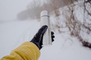 A thermos of gray color in the hand. Hold a flask with a hot drink in your hands. A glass of hot tea. Thermo bottle. photo