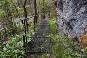 A metal staircase with railings is installed in the park along the rock, a safe passage over the cliff, an iron structure of the descent step, a tourist trail. photo