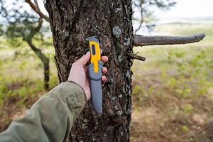 Camping equipment is a knife for survival in the forest, a man's hand holds a gray knife in a sheath. photo