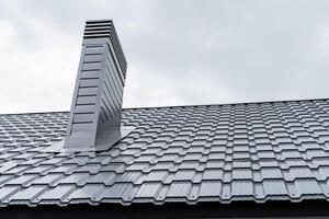 Tiled roof of the new house made of corrugated board, metal coating protection against rain, pipe stands on the roof of the house, smoke extractor, gray metal color photo