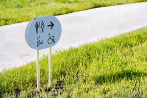 Sign with an arrow towards the toilet, a public restroom for the disabled, a mother-and-child room, a lawn banner, a city toilet, a road in the park. photo