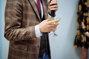 A person's hand holds a glass of wine, gives a speech at a speech, drinks champagne at parties, an engagement ring, a plaid jacket, a shirt sleeve sticks out. photo