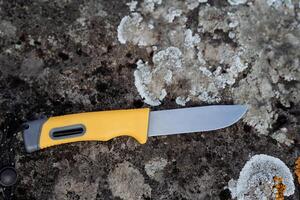 Bushcraft knife with plastic handle, durable steel blade, forest survival knife, blade lying on a stone, hand lanyard. photo