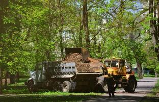 el equipo de mejora de la ciudad quita las hojas caídas en el parque con una excavadora y un camión. trabajo estacional regular en la mejora de los lugares públicos para la recreación foto