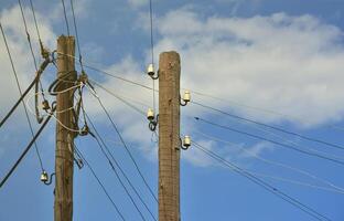 Old wooden electric pole for transmission of wired electricity on a background of a cloudy blue sky. Obsolete method of supplying electricity for later use photo