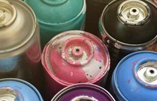 Large number of used colorful spray cans of aerosol paint lying on the treated wooden surface in the artist's graffiti workshop close up. Dirty and stained cans for art photo