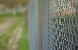 A photograph of a metal net used as a fence of private possessions. Old metal grid in perspective with a blurred background photo