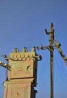 Old and obsolete electrical transformer against the background of a cloudless blue sky. Device for distribution of supply of high-voltage energy photo