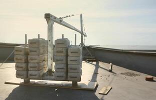 Counter weight or weight balance concrete blocks or bricks as part of suspended wire rope platform for facade works on high multistorey buildings. Many blocks with metal handles photo