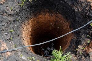 un agujero excavado para un Bueno, un profundo redondo Bueno, un alcantarilla, un jardín alcantarillado, perforación, goteo el suelo. foto