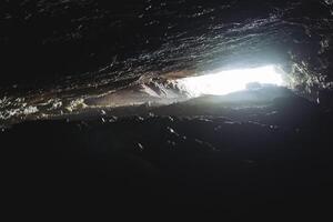 Cave light at the end of the passage, narrow underground manhole, overhanging vaults of the cave grotto, bright spot of light, speleology in section. photo