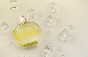 Female perfume yellow bottle, Objective photograph of perfume bottle in ice cubes and water on white table. View from above. Mockup product photo, concept of freshness photo