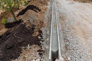 A direct rainwater drainage line, a sewage ditch, roadworks, asphalt laying, a layer of rubble on the road, a sidewalk curb. photo