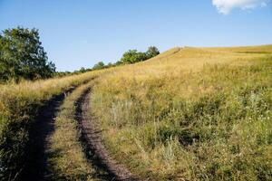 Dirt road steeply rises up the field, mountainous terrain, evening landscape, smooth turn of the road, horizon line, at the top of the mountain, Russian field photo