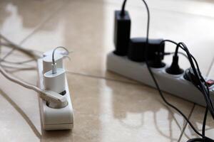 Overloaded power boards. Power strips with different electrical plugs on white floor photo