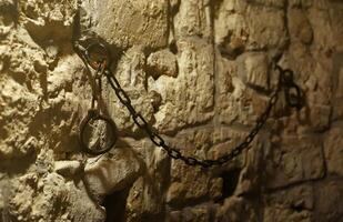 Slavery and bondage strong steel old shackles on stone wall in castle cellar photo