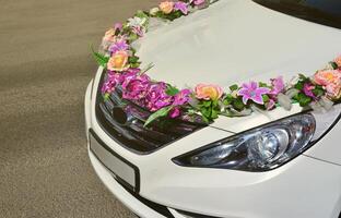 una foto detallada del capó del coche de la boda, decorado con muchas flores diferentes. el coche está preparado para una ceremonia de boda