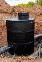 A black well stands in the ground, a deep clay pit under the pipeline, a hydropower supply unit of the city, a concrete well, bitumen protective properties against erosion. photo